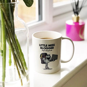 A mug on a windowsill which reads Little Miss Blogger with a character holding a laptop