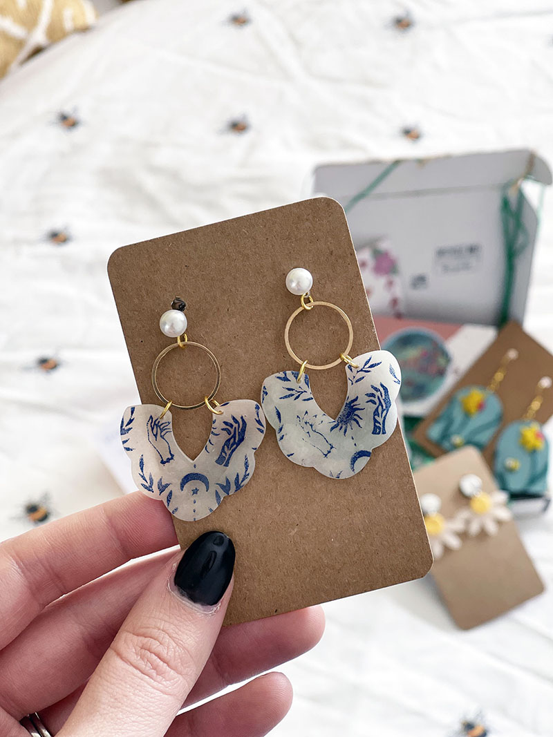 pair of white and blue hanging earrings with gold hardware and a pearl stud, finished off with a tarot reading print. Attached to a brown backing card