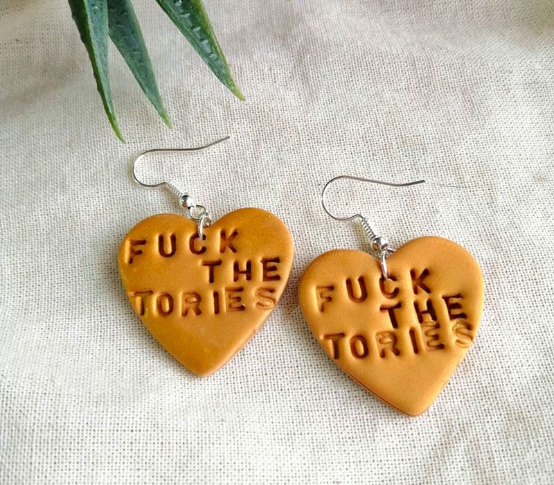 Heart-shaped earrings stamped with the words Fuck the Tories