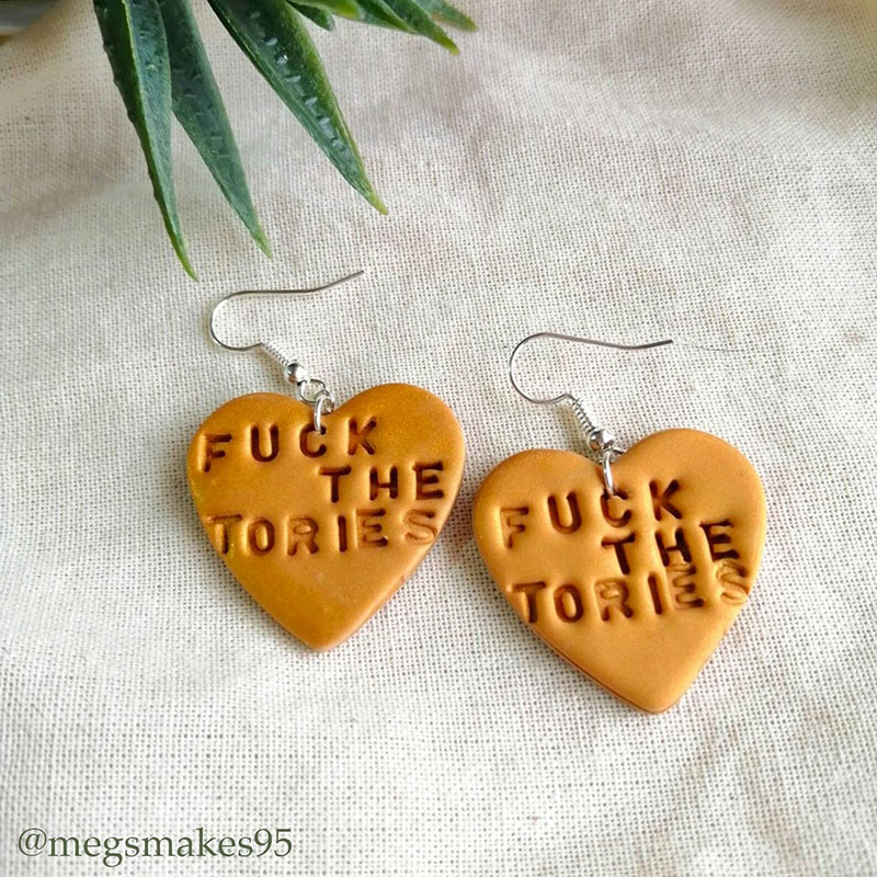 Heart-shaped earrings stamped with the words Fuck the Tories