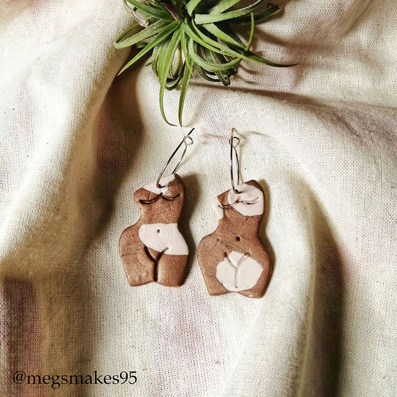 a pair of brown and white earrings in the shape of a naked female body, laid on some cloth