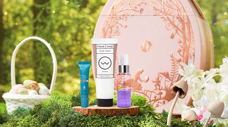 three beauty and haircare products sat on a piece of rustic wood on some grass, in front of a pink egg shaped box