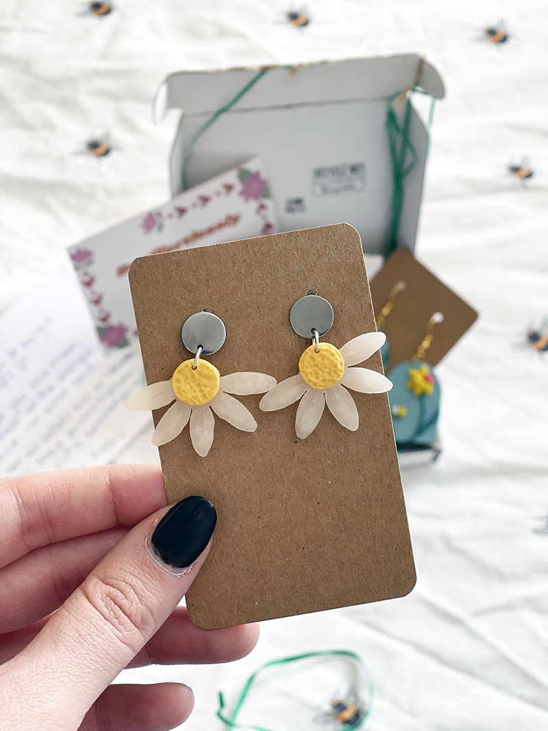 pair of hanging earrings in the shape of daisy petals with a silver stud. Attached to a brown backing card.