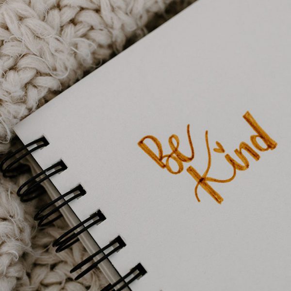 notebook with gold calligraphy writing inside reading Be Kind