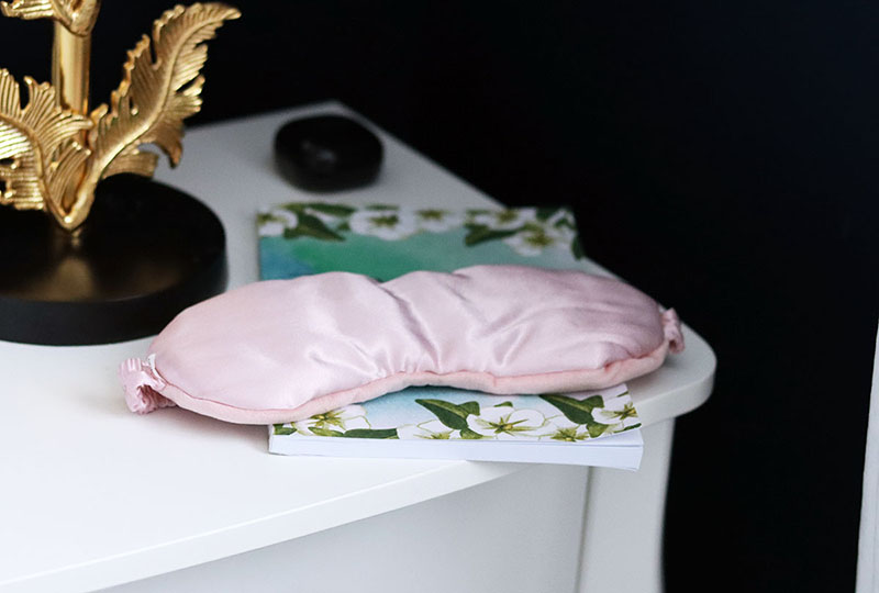 pink silk weighted eye mask sat on top of a journal on a bedside table