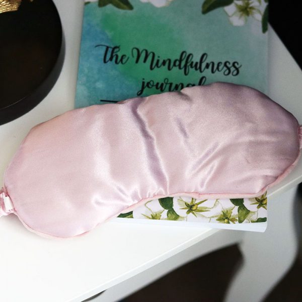 pink silk weighted eye mask sat on top of a journal